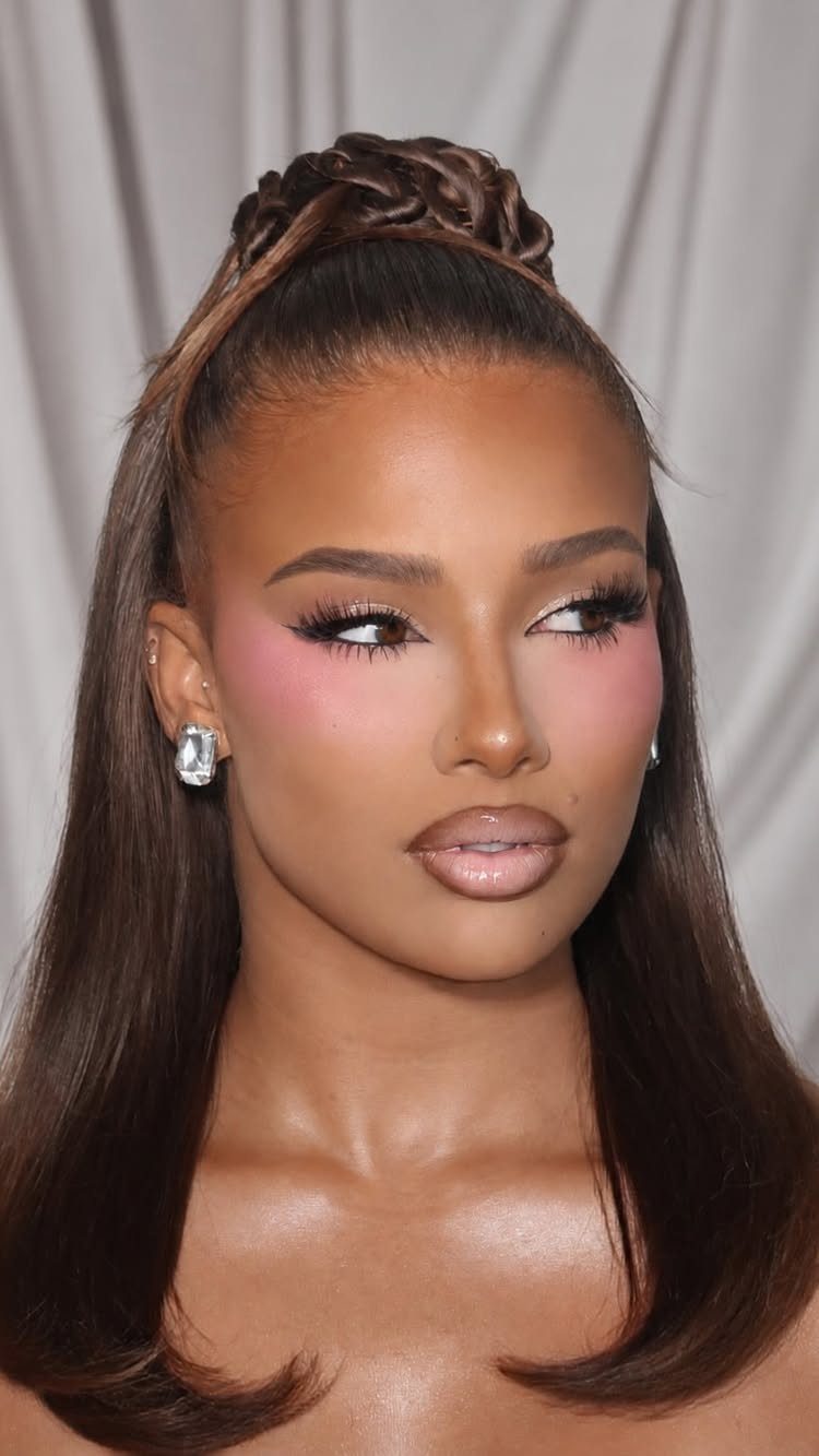 Woman with a high ponytail wearing bold pink blush and glossy nude lips.