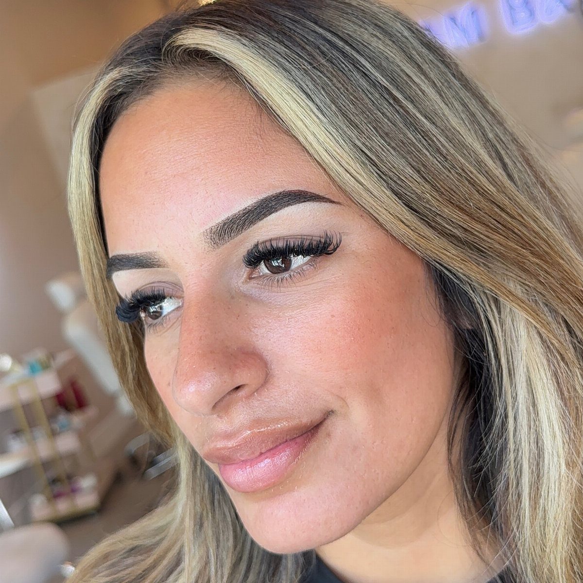 Woman with defined bold eyebrows, long lashes, and glossy pink lips posing.