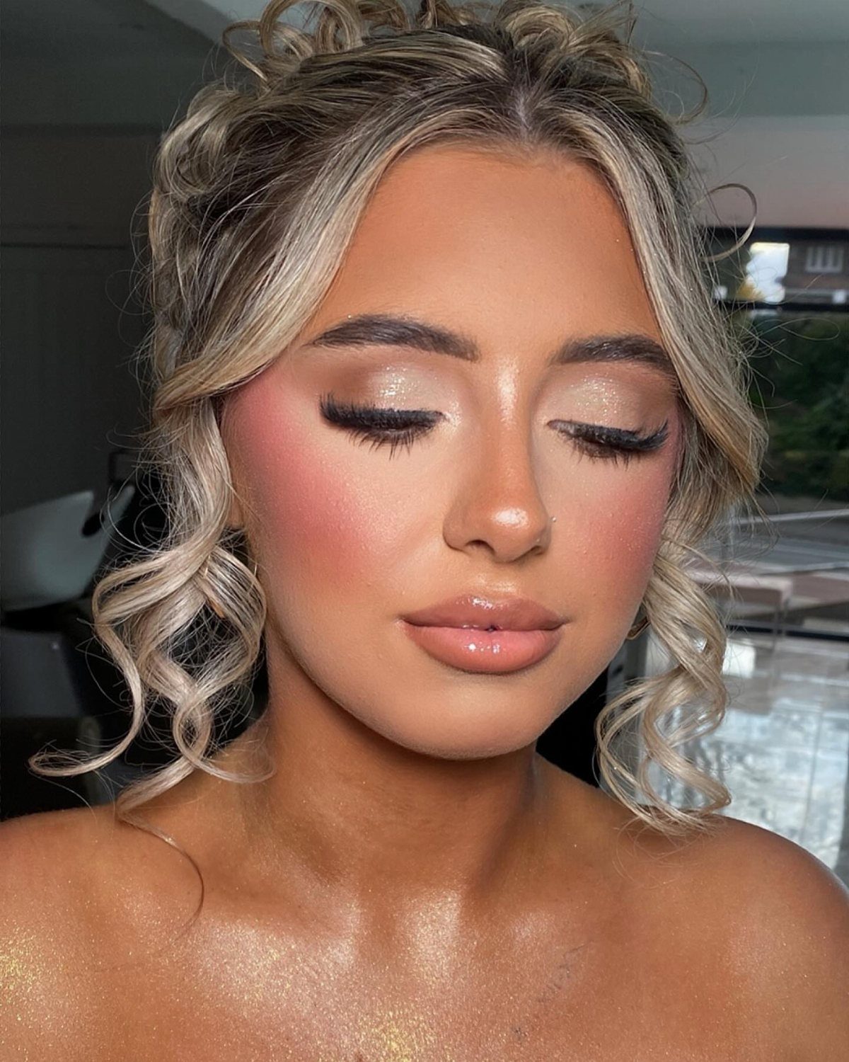 Woman with bronzed glowing skin, shimmering eyeshadow, and glossy lips posing for portrait