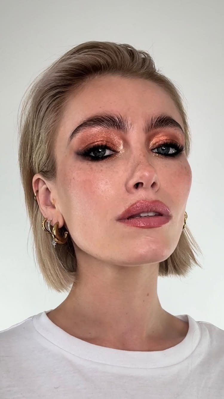 Woman with shimmering copper eyeshadow, bold brows, and glossy pink lips posing.