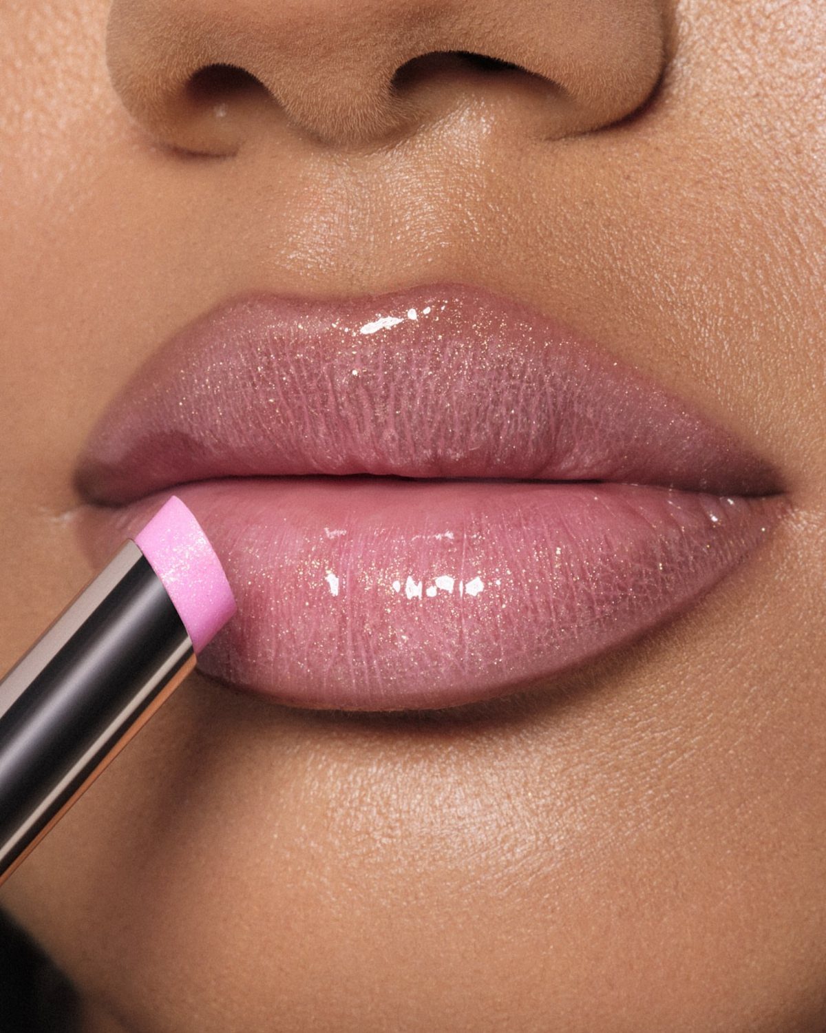 Light pink glossy lips being applied with a lipstick applicator in close-up.