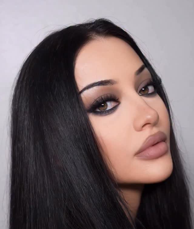 Woman with long black hair wearing brown smokey eyeshadow and matte nude lips.