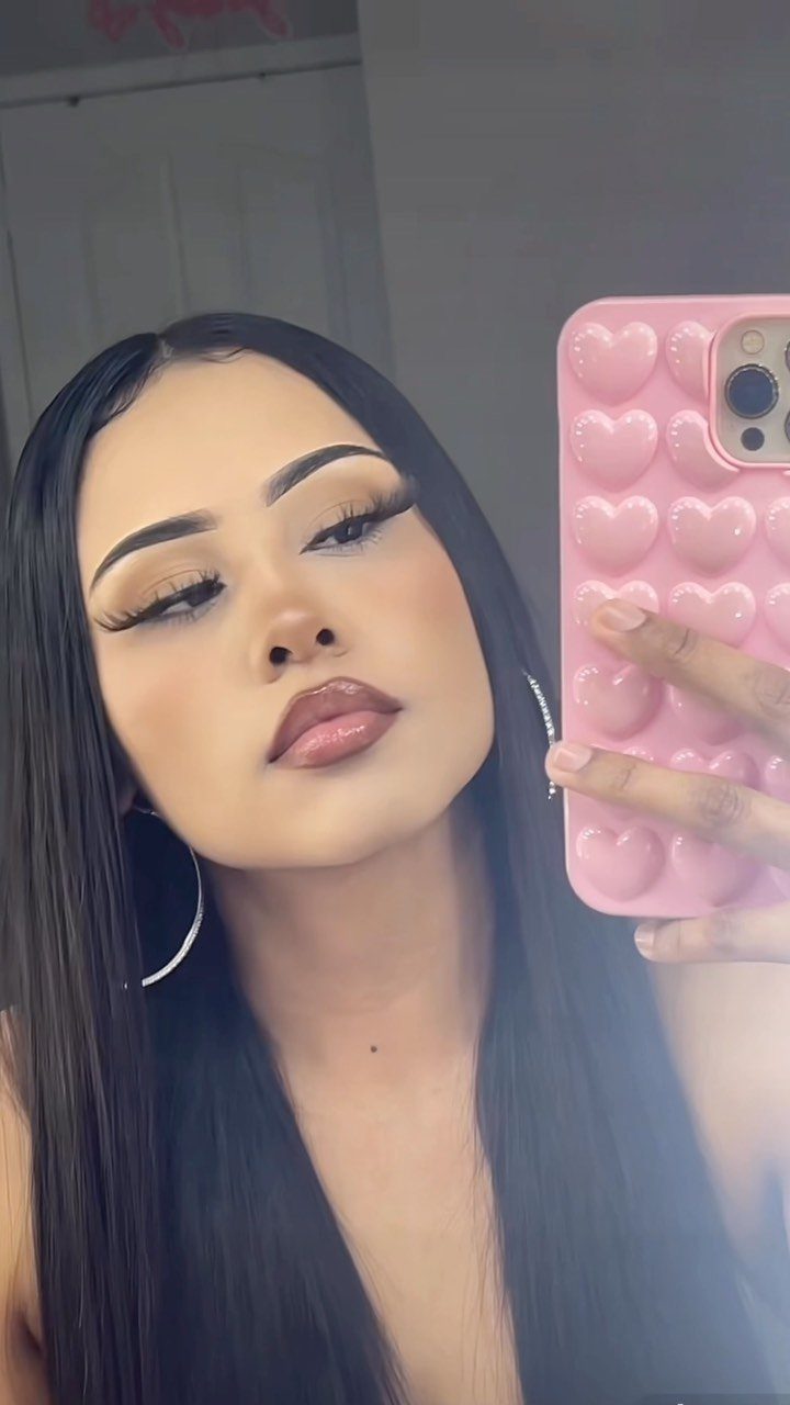 Woman with defined brows and full glam makeup taking a mirror selfie