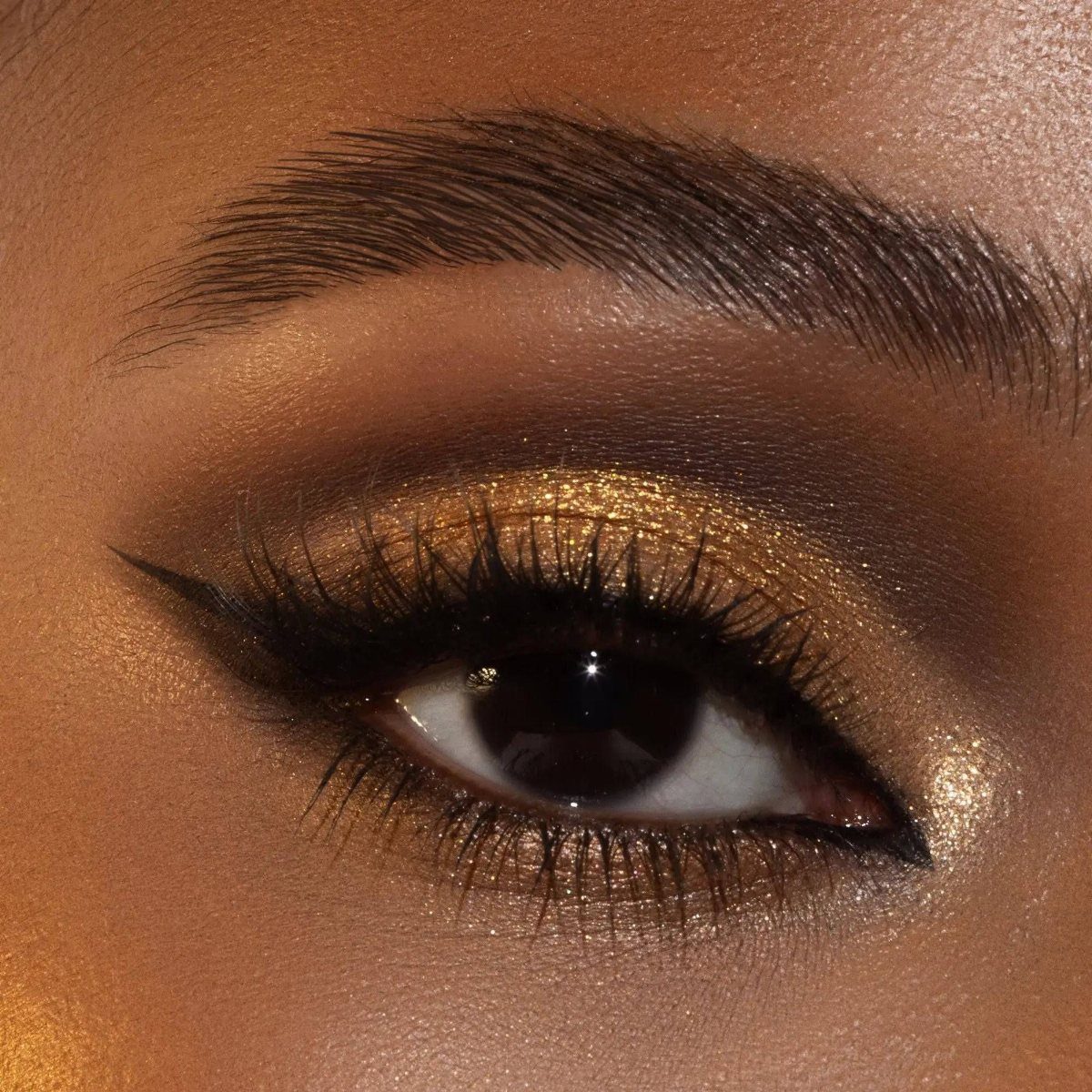 Eye with gold shimmer eyeshadow, winged black eyeliner, and voluminous black lashes.
