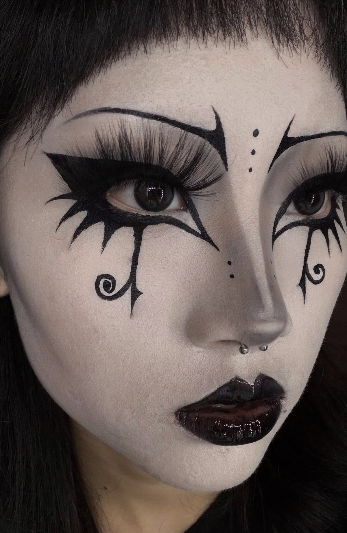 Person with pale skin wearing dramatic black graphic eyeliner and dark glossy lips.