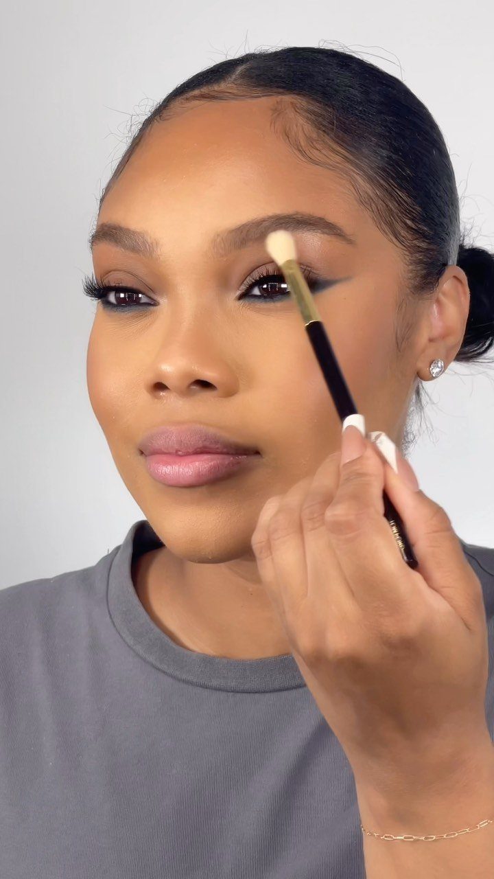 Black Skin Makeup Ideas: 8 Looks From Bronzer to Glossy Lips 5 Woman with dark skin showing winged eyeliner while a brush touches her brow.