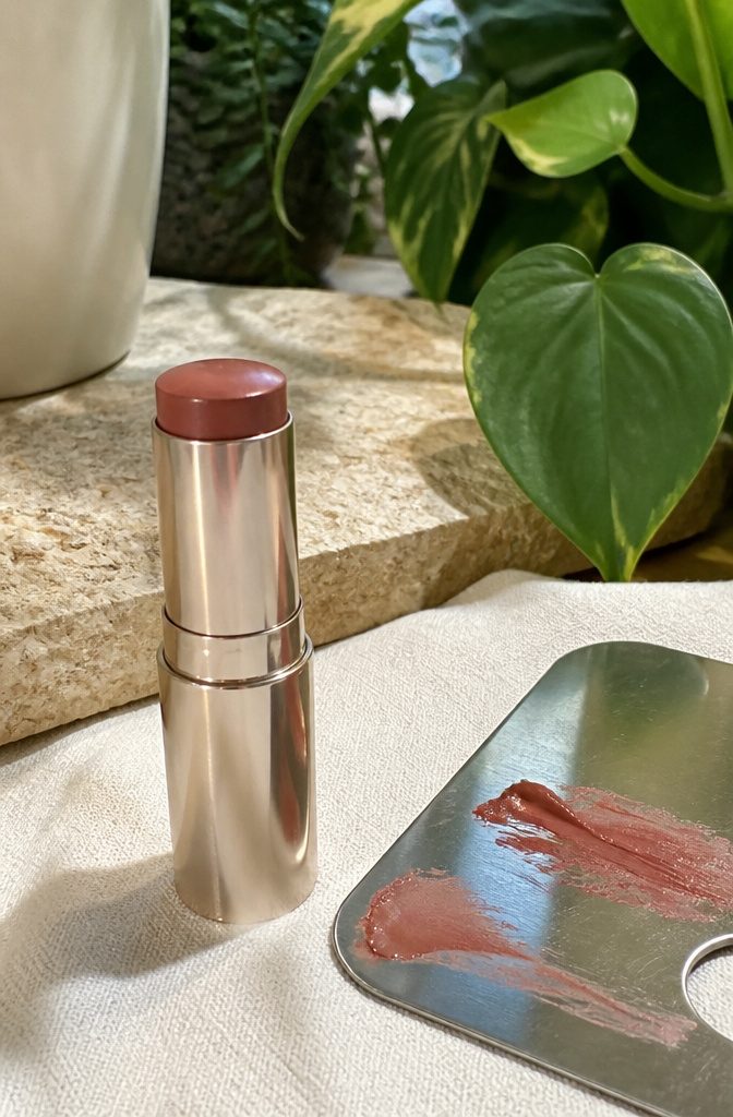 Haus Labs Color Fuse Glassy Blush Balm Stick in Clove against a stone background.