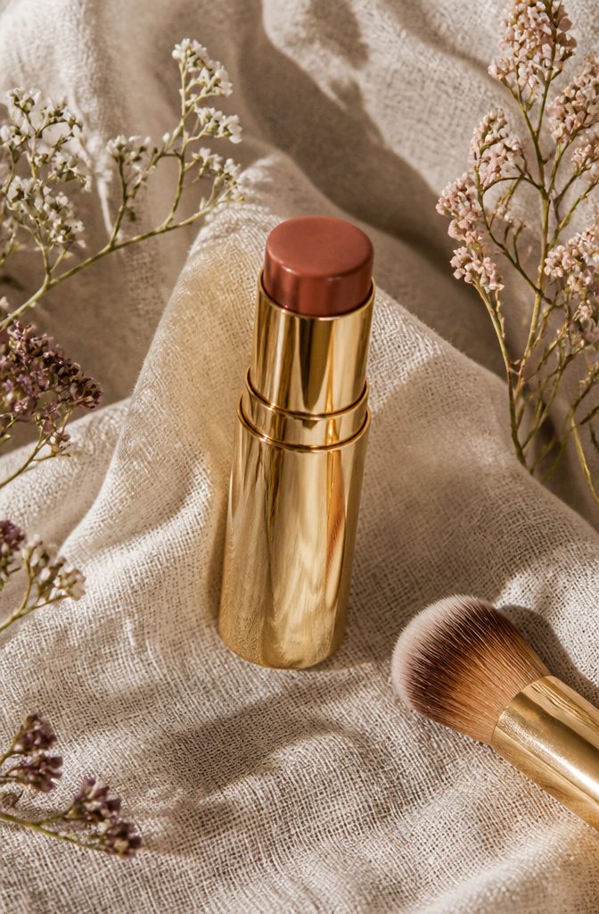 Merit Flush Balm in Terracotta displayed with muted wildflowers.