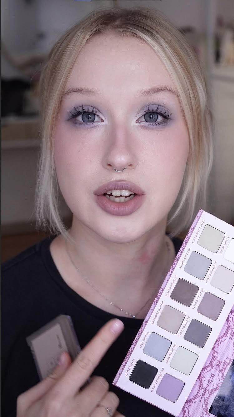 Woman with cool toned purple eyeshadow holding a grey and purple eyeshadow palette.