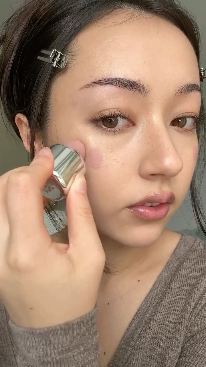 Woman applying pale pink blush to her cheek with a silver makeup stick.