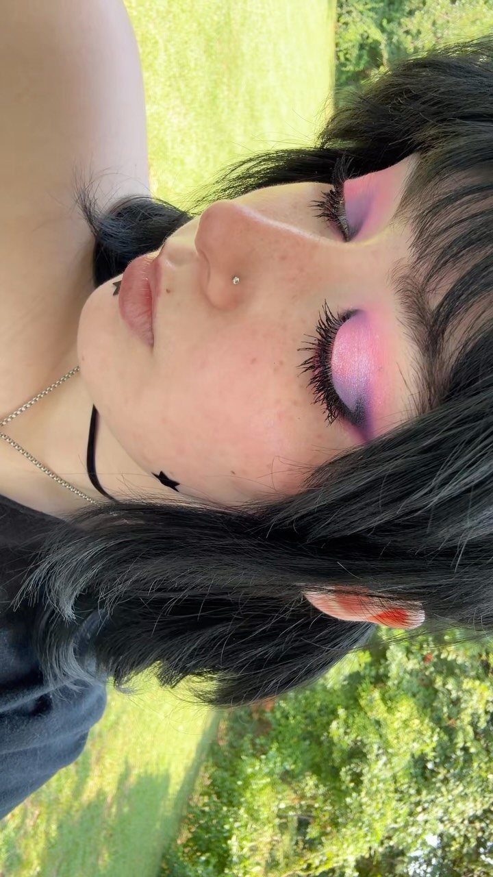 Person with black hair wearing pink and purple eyeshadow and long eyelashes.