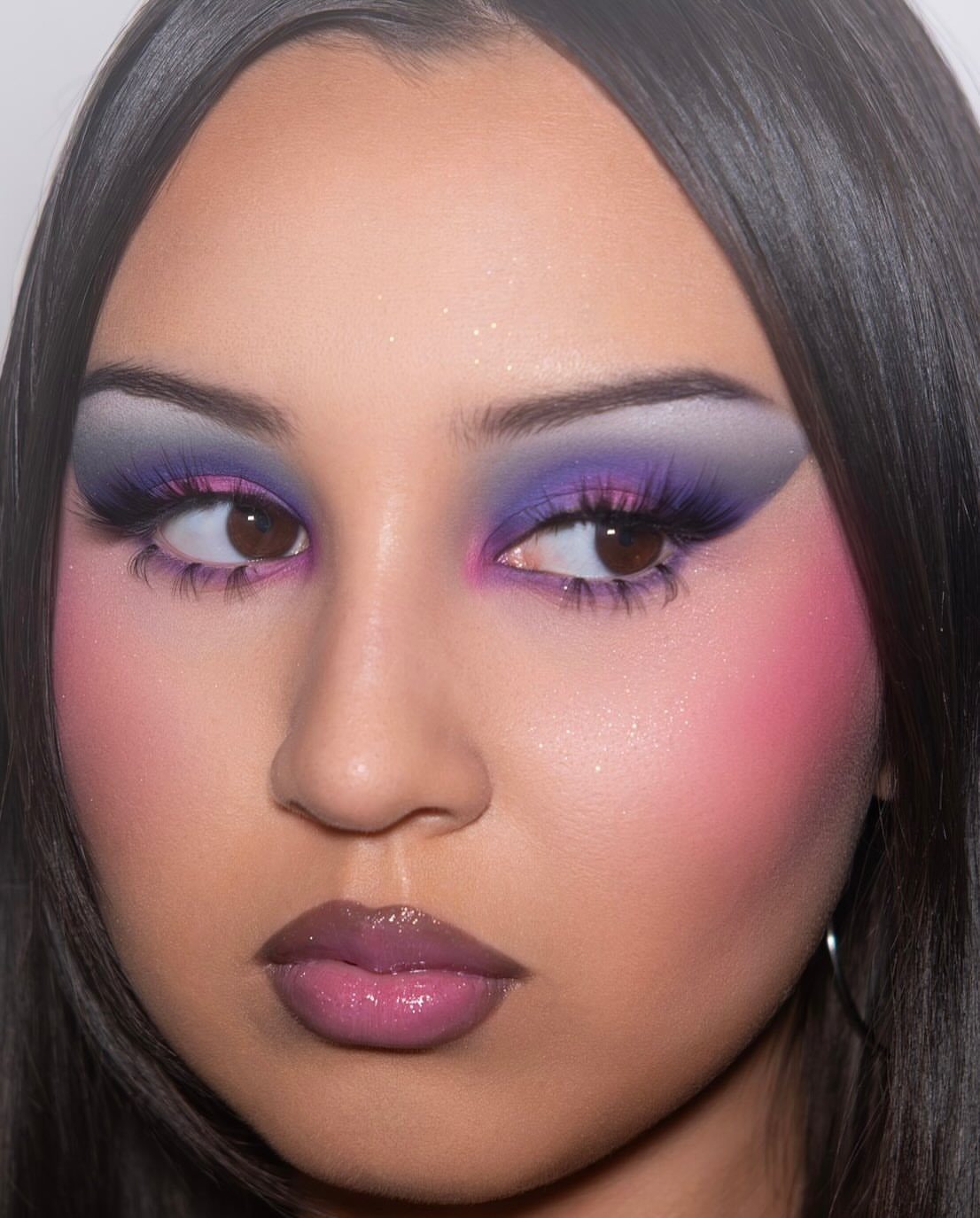Person with dark hair wearing bold purple eyeshadow, pink blush, and mauve lipstick.