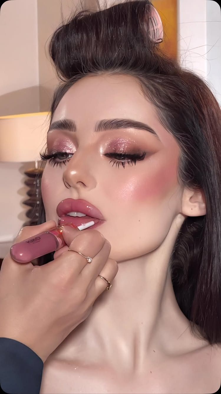 Woman receiving glossy pink lipstick application with full glam makeup and glittery eyes