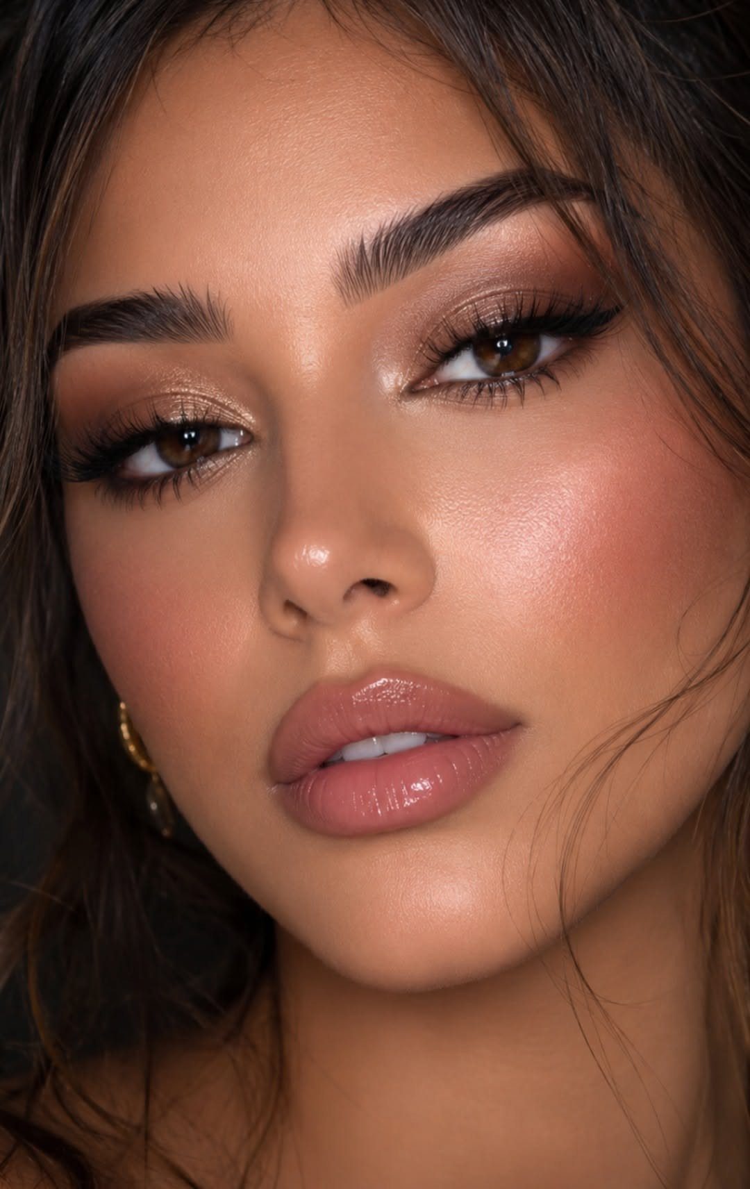 Woman with glossy nude lips, winged eyeliner, and shimmery gold eyeshadow makeup.