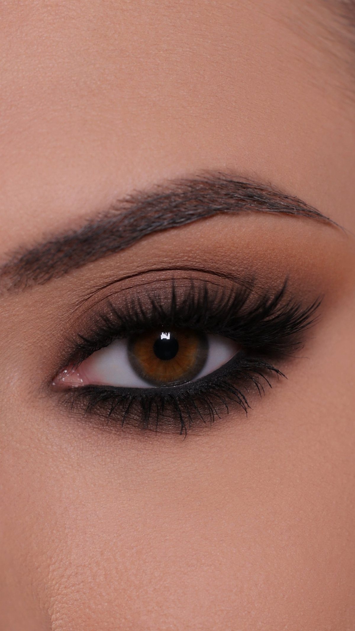 Eye with neutral brown eyeshadow, winged black eyeliner, and long voluminous lashes.