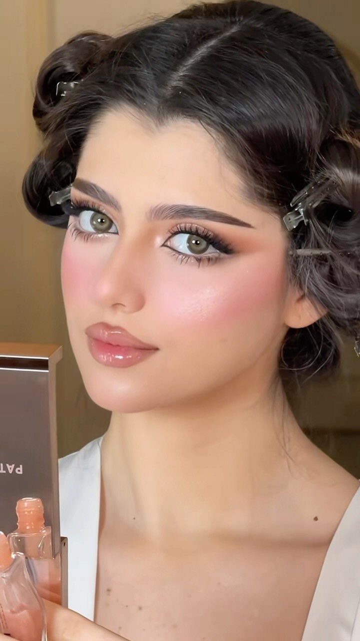 Woman with glam makeup featuring prominent peach blush and winged black eyeliner.
