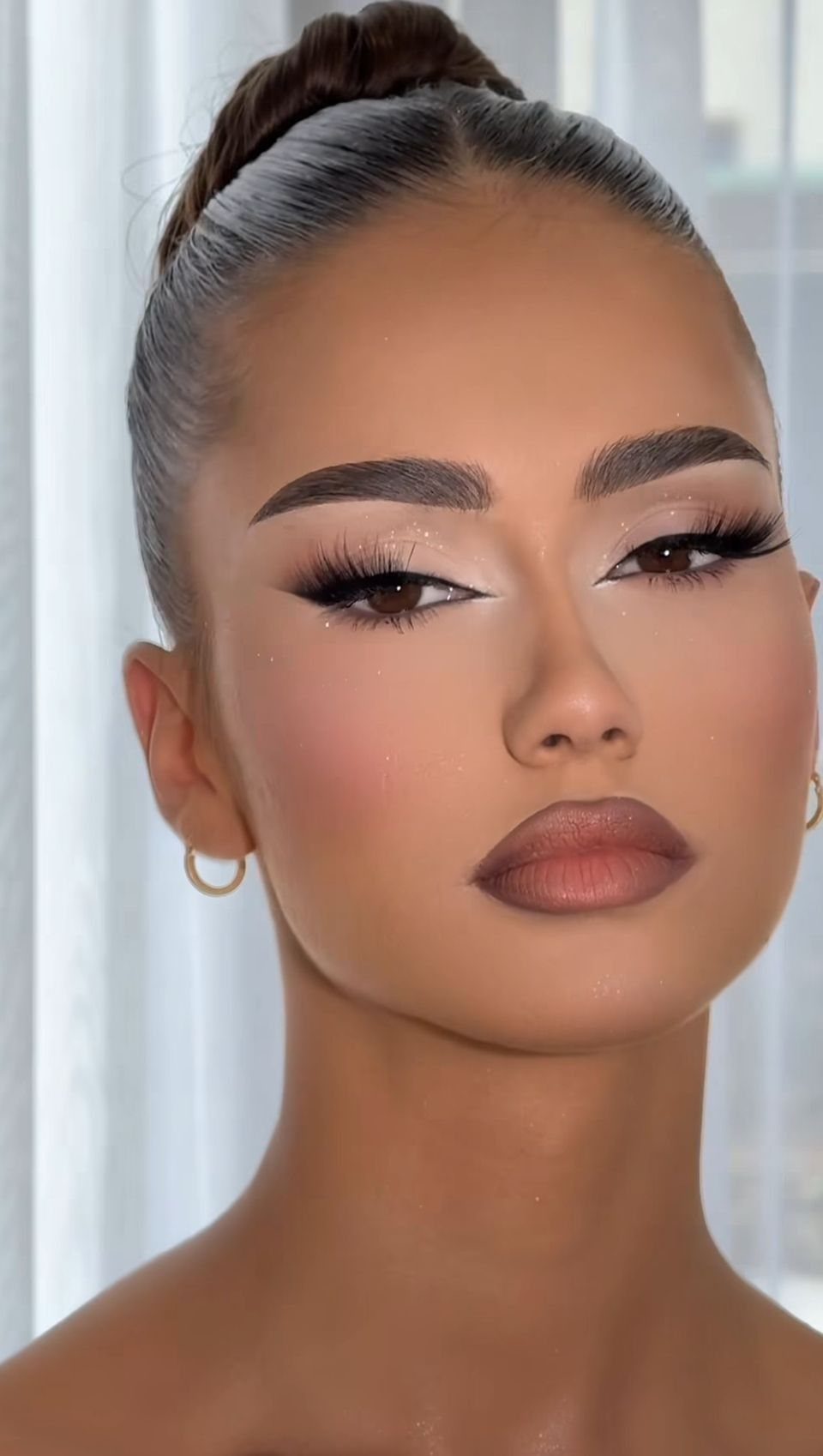 Woman with sculpted brows, winged eyeliner, and matte brown lipstick in a portrait.