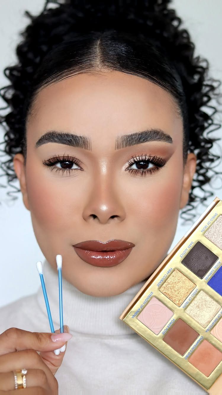Woman with foxy eye makeup holding cotton swabs and a gold eyeshadow palette