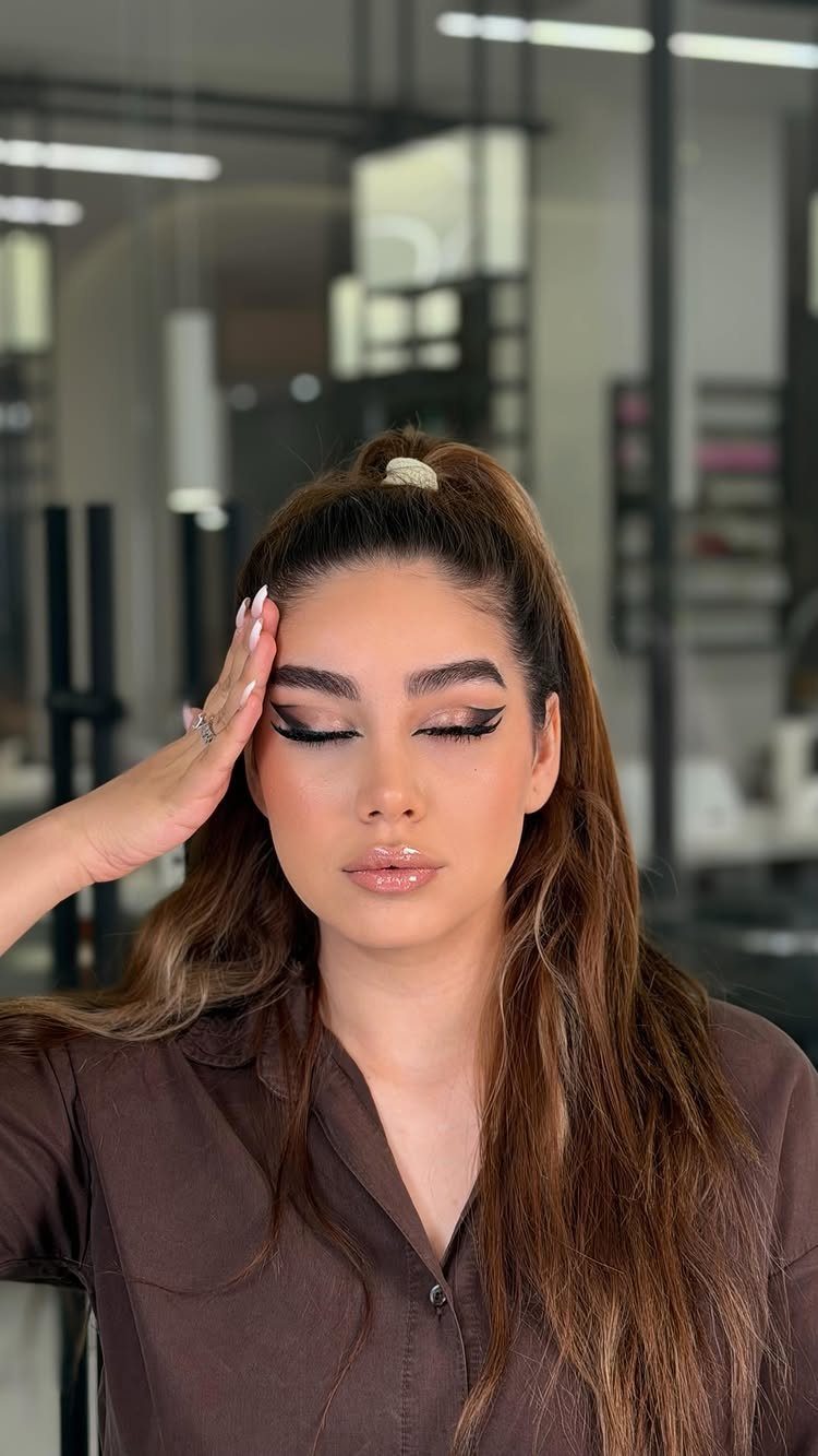 Woman with glam makeup featuring sharp black winged eyeliner and glossy nude lips.