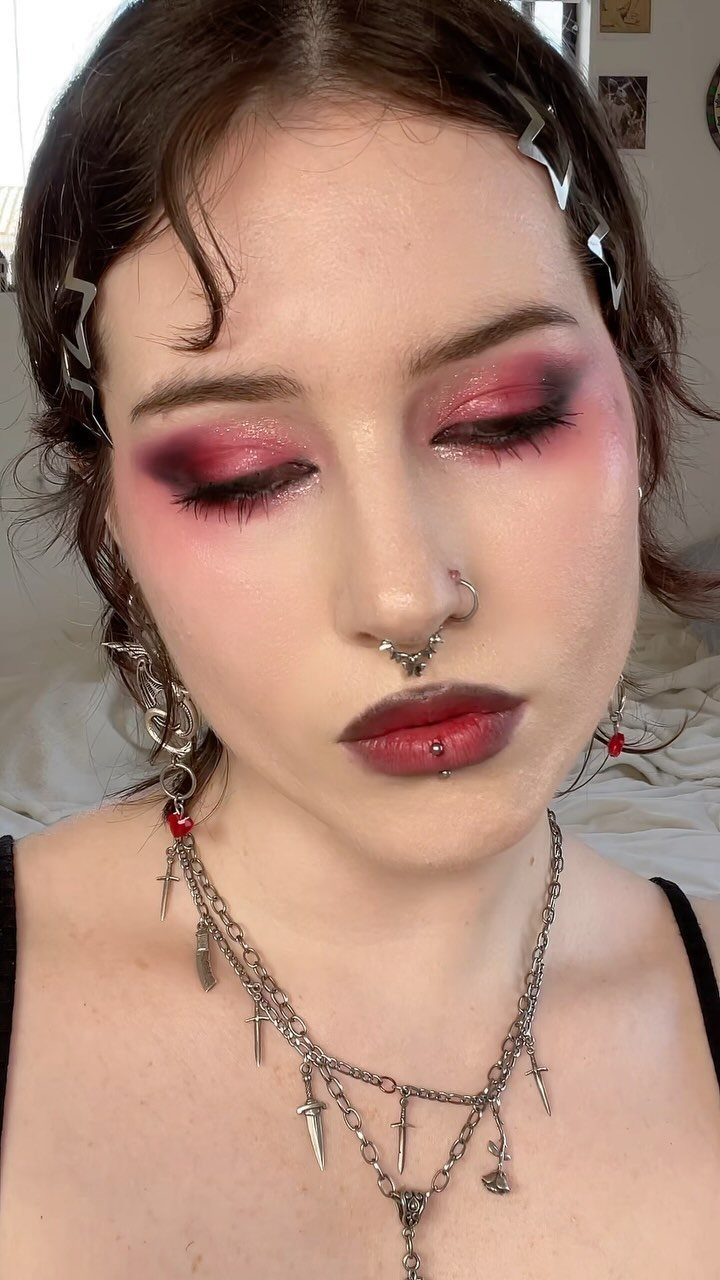 Person with dark red lips, red smokey eyeshadow, and silver facial piercings.