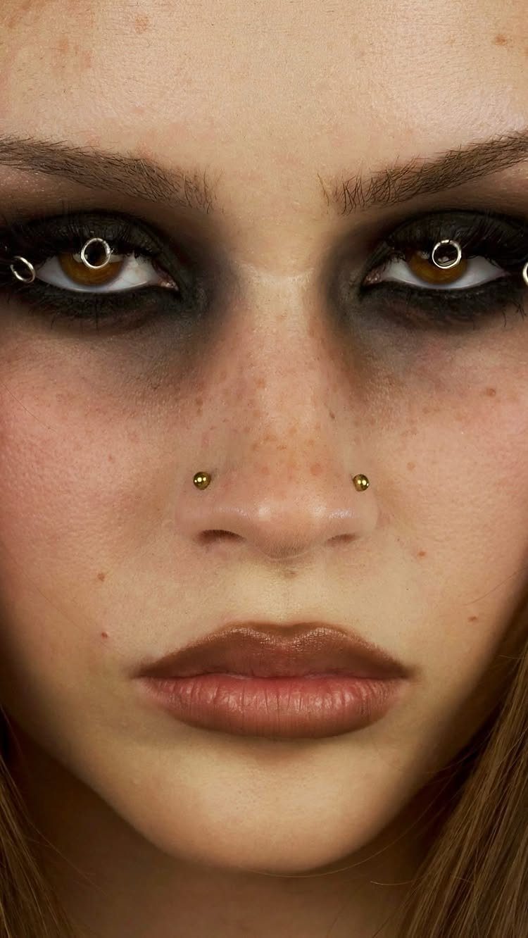 Person with heavy black smokey eye makeup and facial piercings on nose and eyelids
