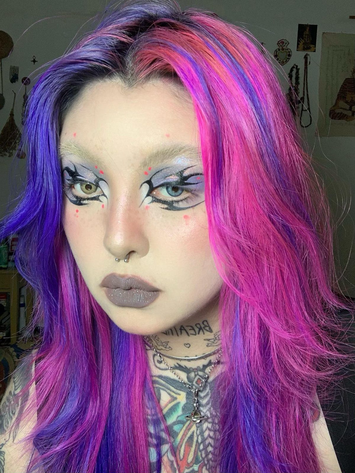 Person with pink and purple hair wearing intricate geometric black eyeliner and grey lipstick