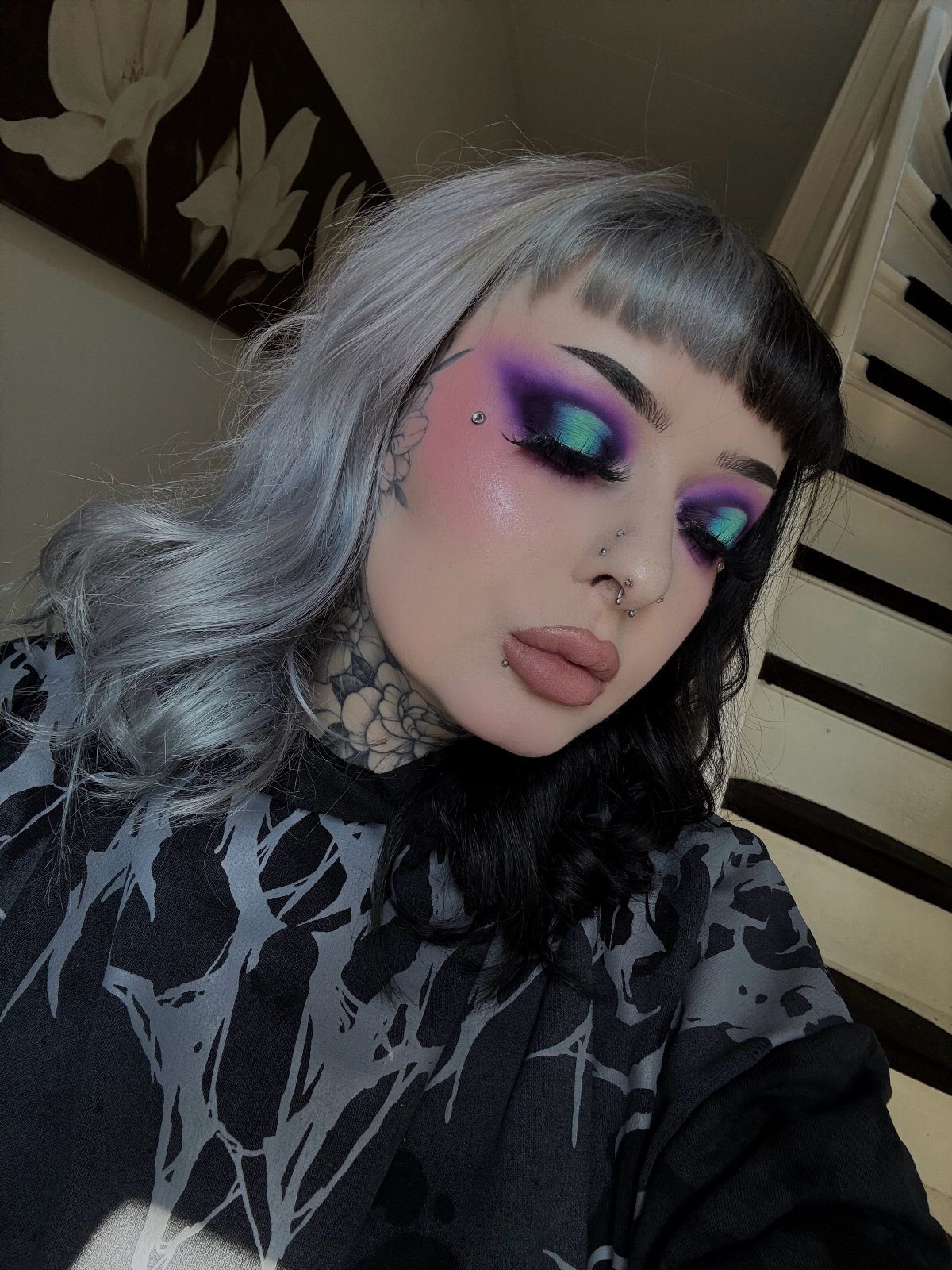 Person with split silver and black hair wearing bold purple and teal eyeshadow