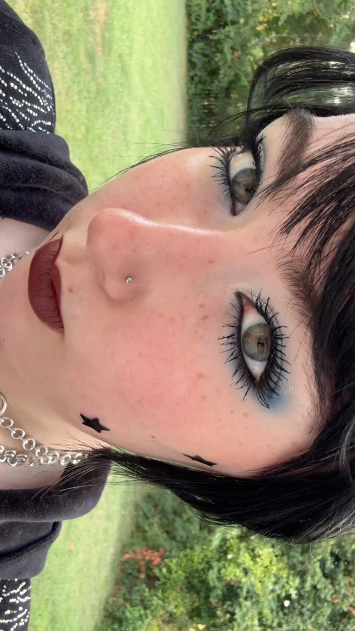 Person with emo makeup featuring thick black mascara and dark red lips.