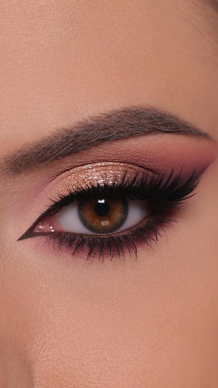 Close-up of eye with shimmering gold and pink dramatic makeup and winged eyeliner