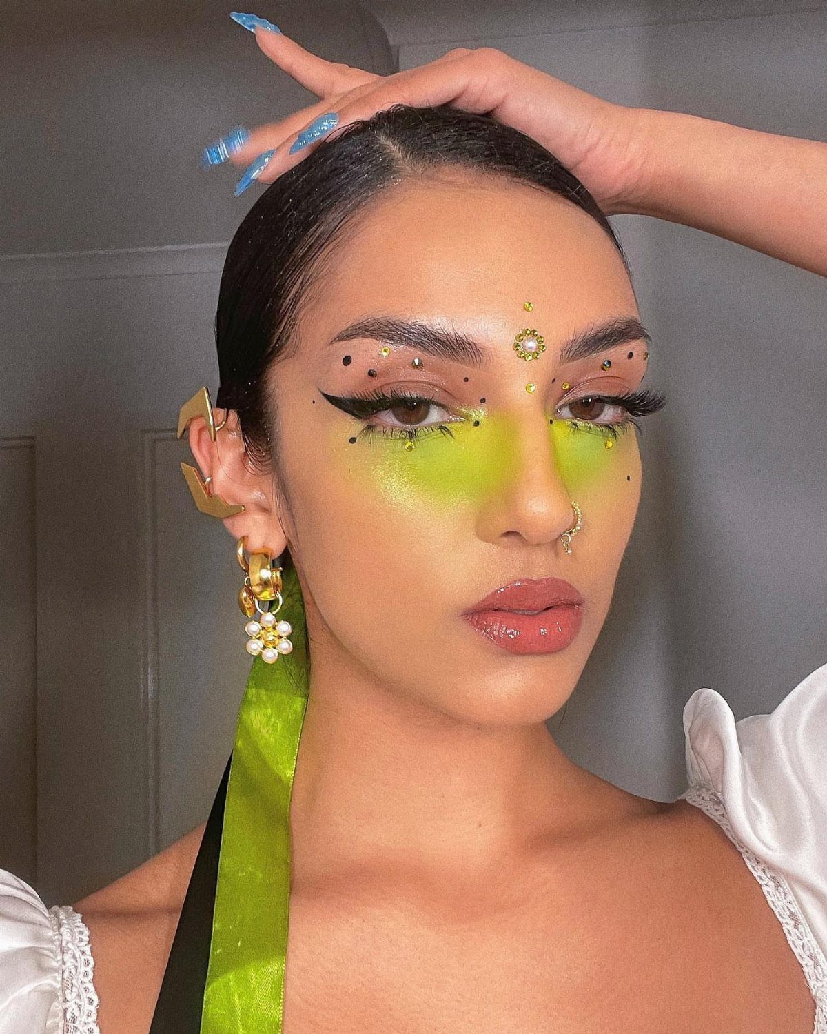 8 Eye Gem Ideas for Sparkly Party Makeup Looks 5 Woman with green eyeshadow and small black gems around her eyes and cheeks.