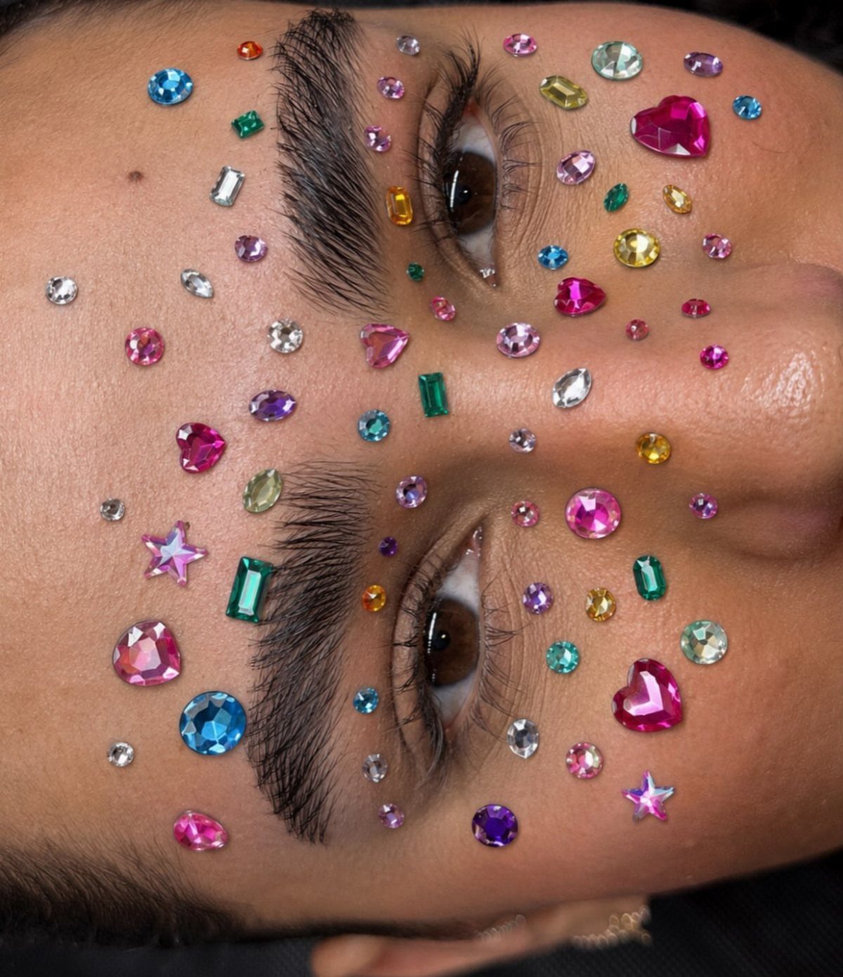 8 Eye Gem Ideas for Sparkly Party Makeup Looks 1 Colorful rhinestones and gems applied around the eyes and eyebrows of a person