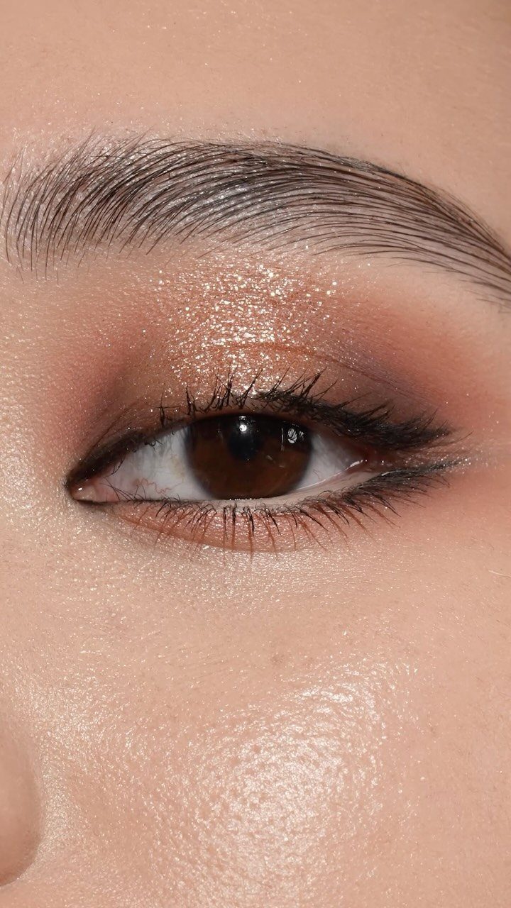 Eye with shimmering gold eyeshadow, thin eyeliner, and glowing skin highlight.