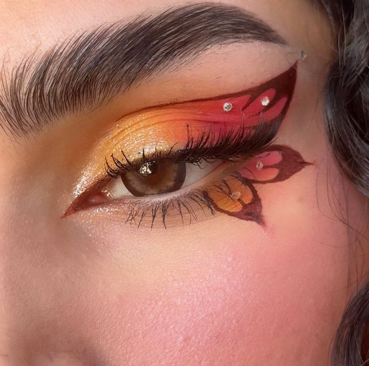Eye with artistic butterfly wing makeup in orange, red, and yellow tones.