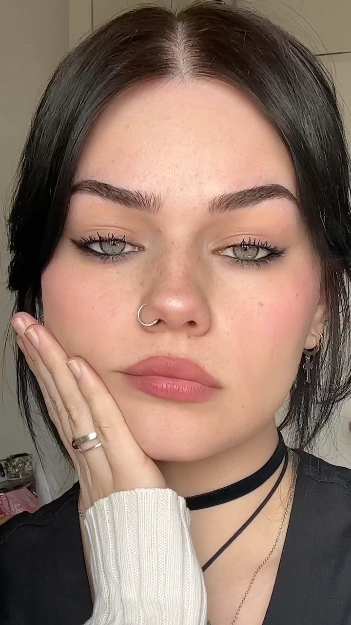 Woman with sharp black winged eyeliner, dark hair, and a nose ring posing.