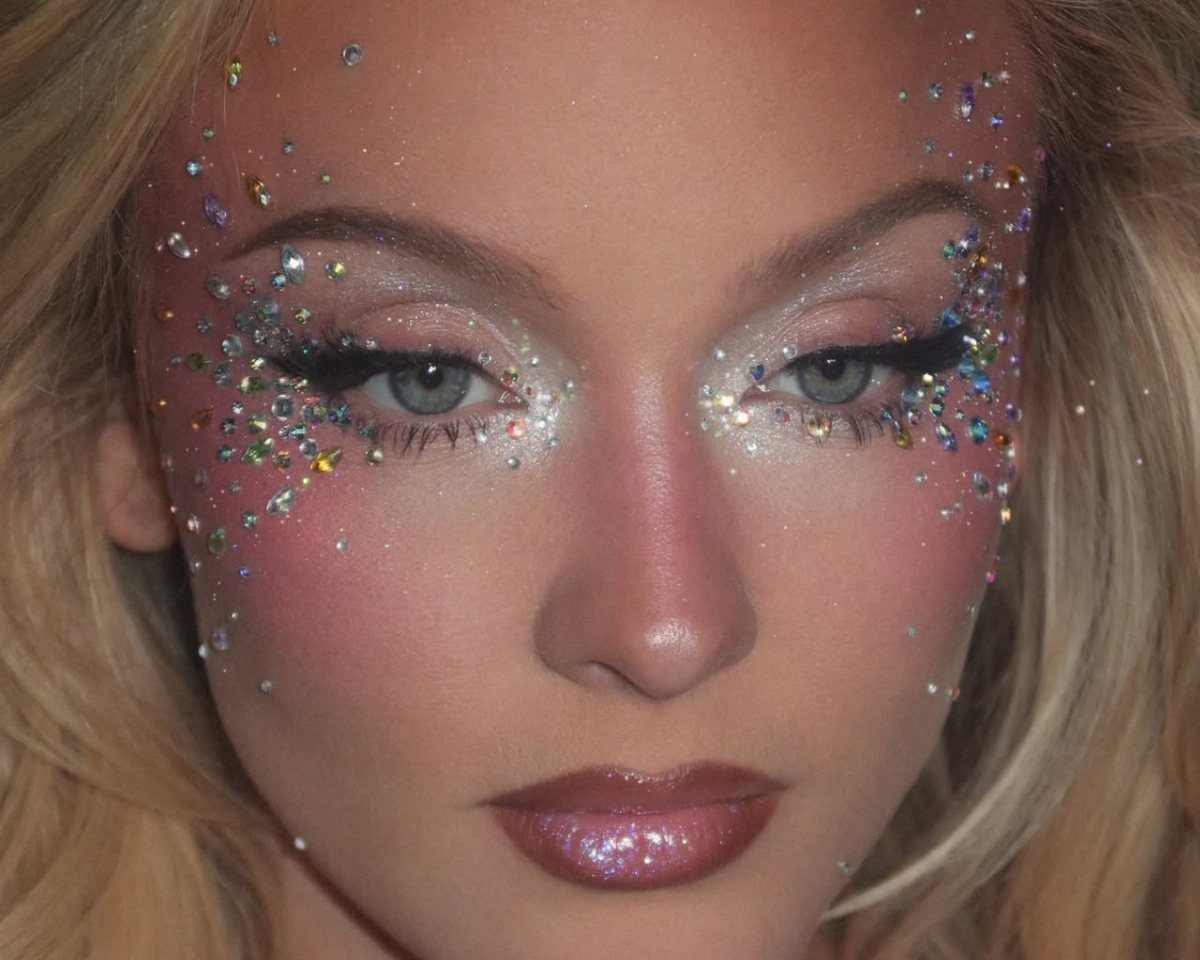 Woman with iridescent rhinestones and gems applied around her eyes and cheeks.