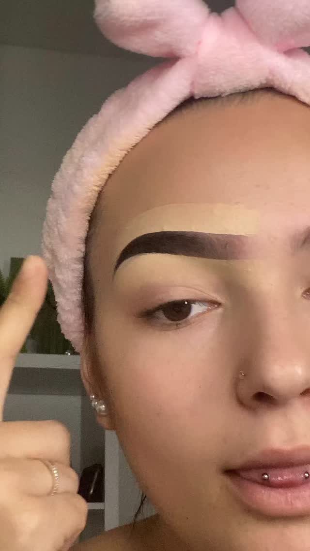 Person with a pink headband showing a shaped, filled-in eyebrow with concealer above.