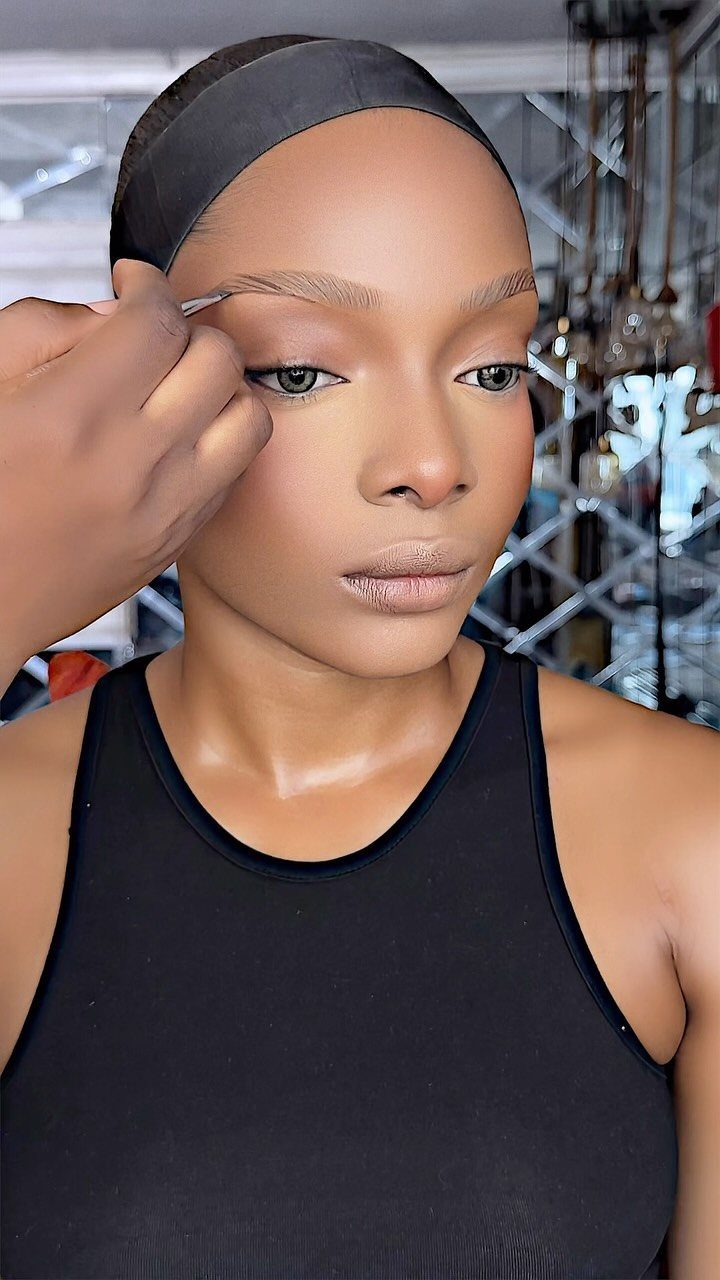 Woman receiving eyebrow makeup application with a small brush in a studio setting.
