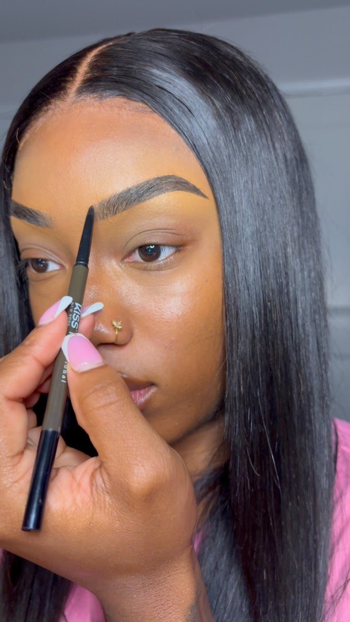 Woman using a brown pencil to shape and fill in her eyebrows.