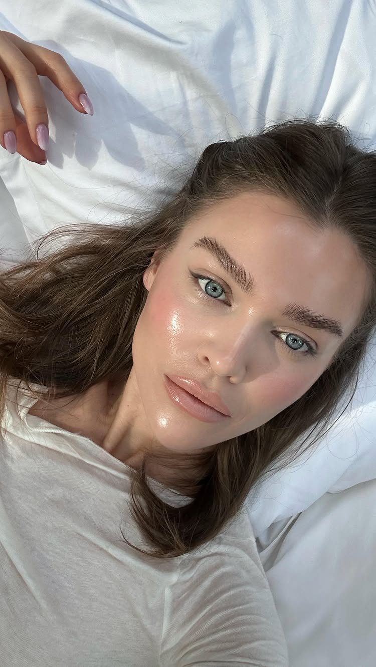 Woman with groomed brown eyebrows and blue eyes lying on white sheets