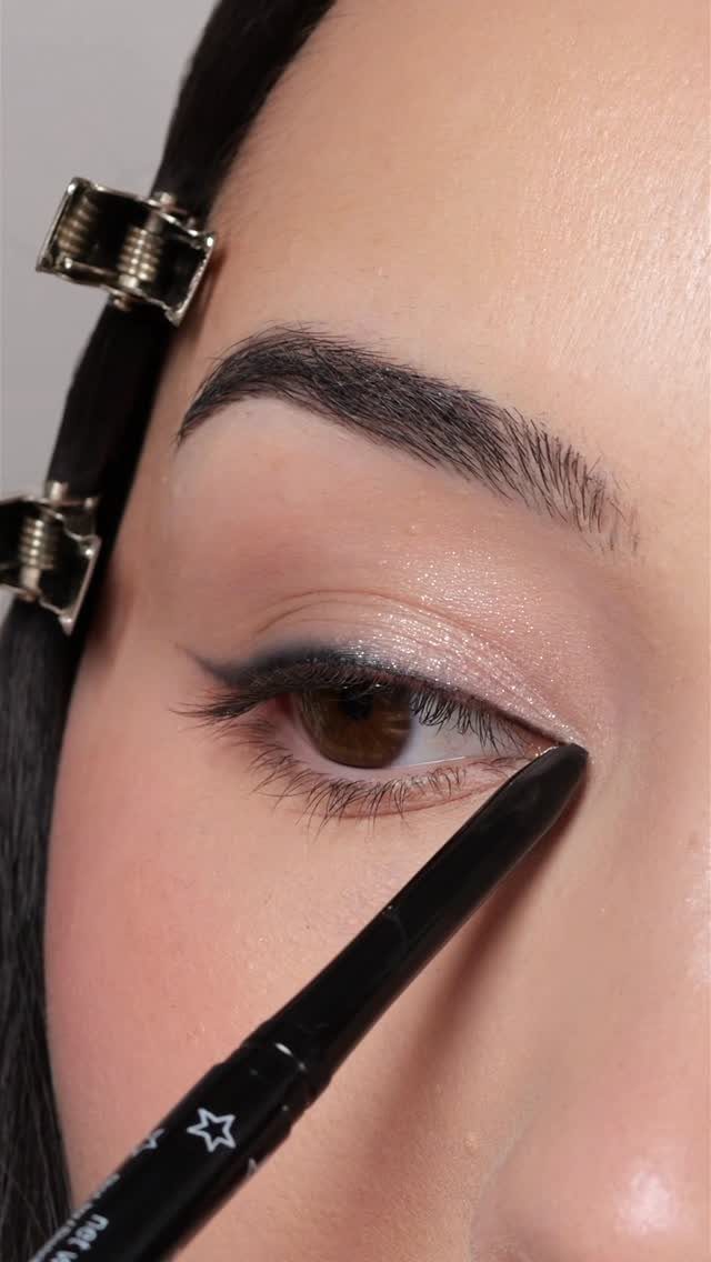 Close-up of an eye with shimmering eyeshadow and black eyeliner pencil application.