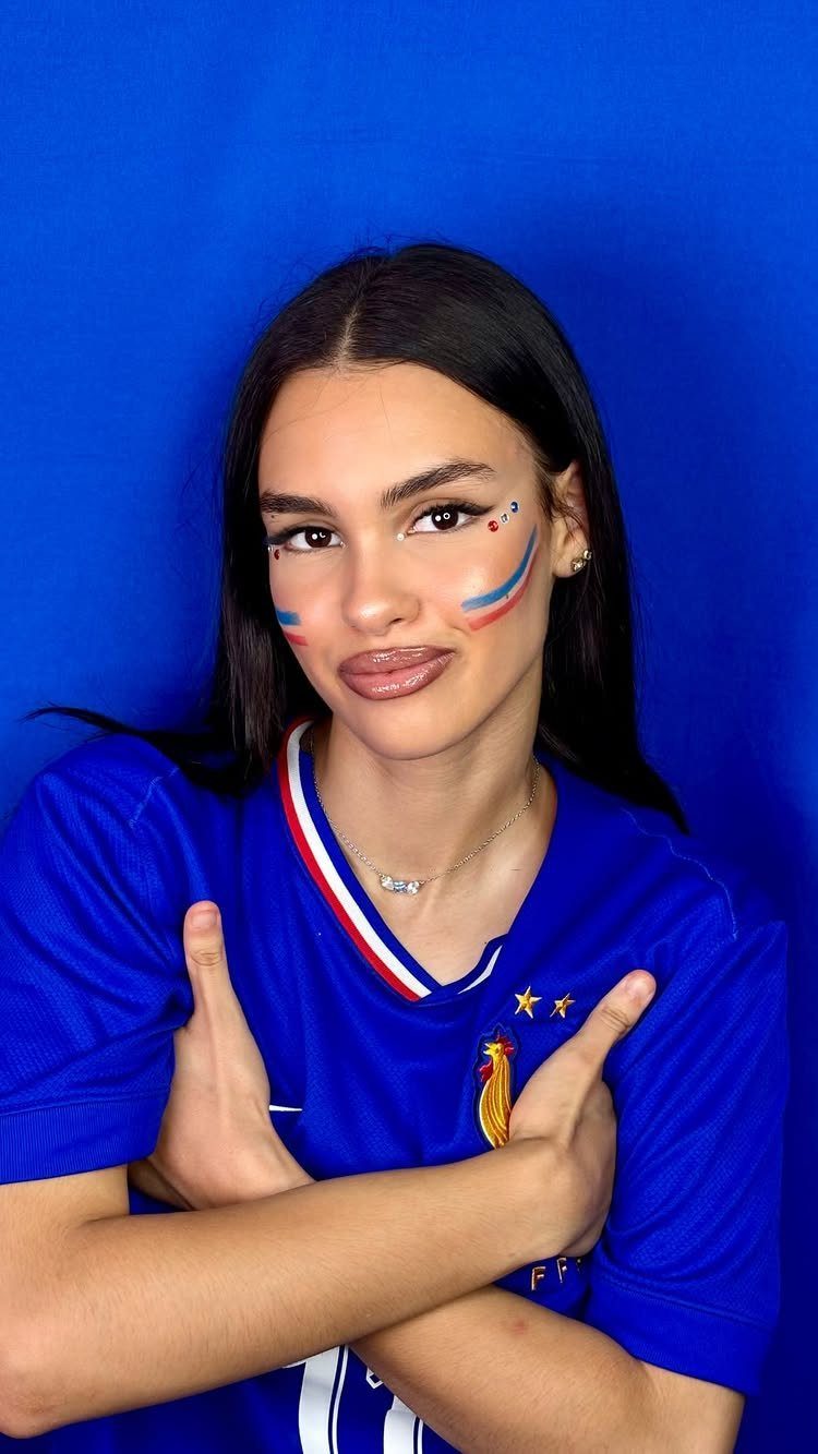 Woman in blue football jersey with French flag face paint posing against blue background