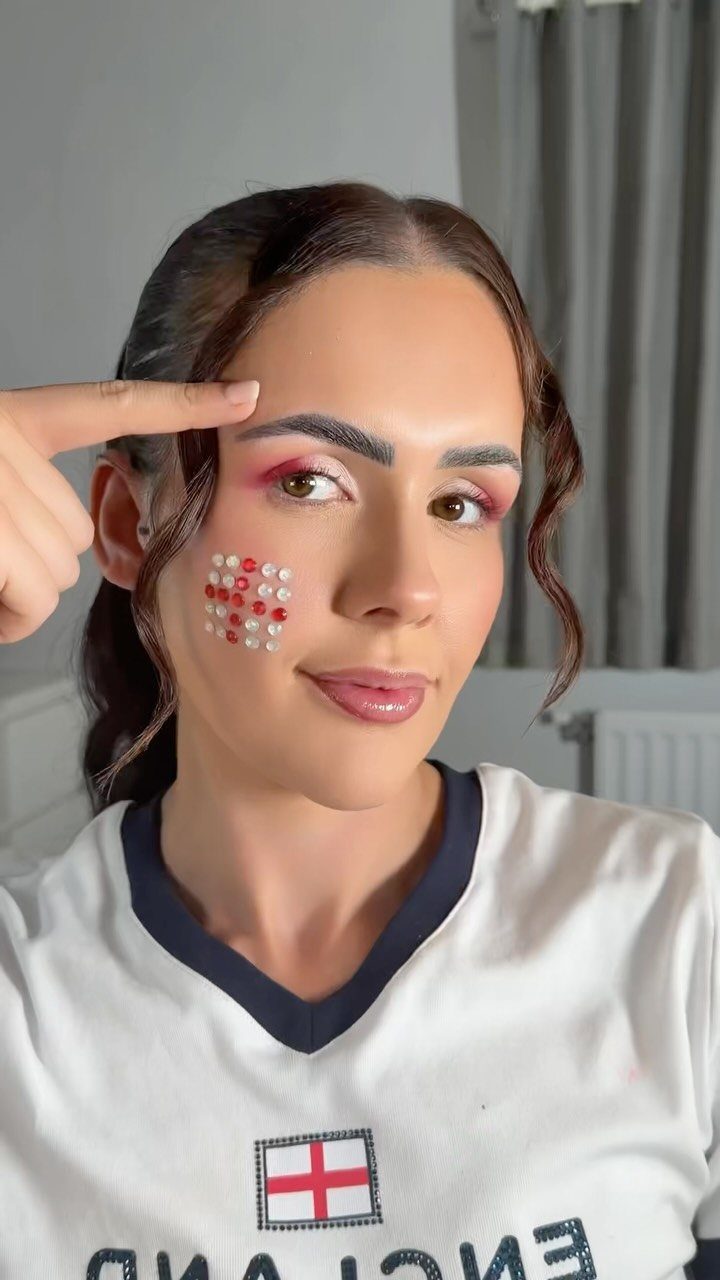 Woman in England football jersey with red and white gem makeup on cheek