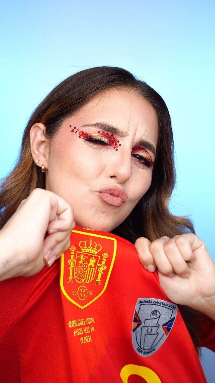 Woman in red Spain football jersey with red and gold glitter eye makeup.