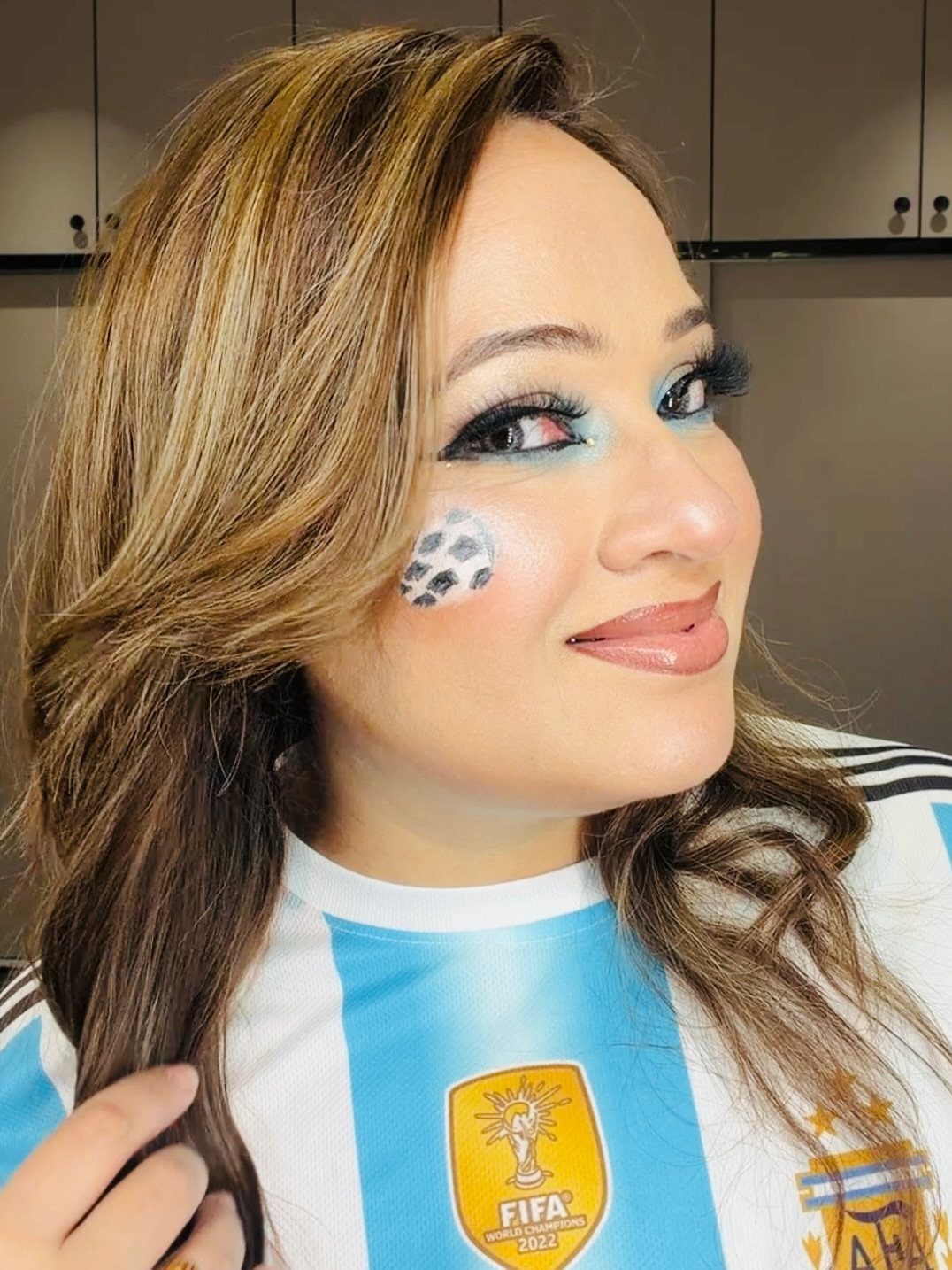 Woman wearing a FIFA jersey with blue eyeshadow and face paint on her cheek