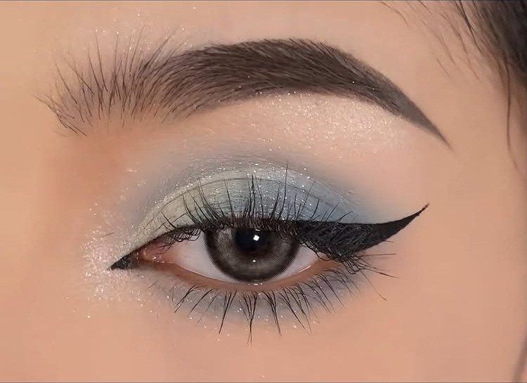 Eye with baby blue eyeshadow, black winged eyeliner, and shimmering silver glitter accents.