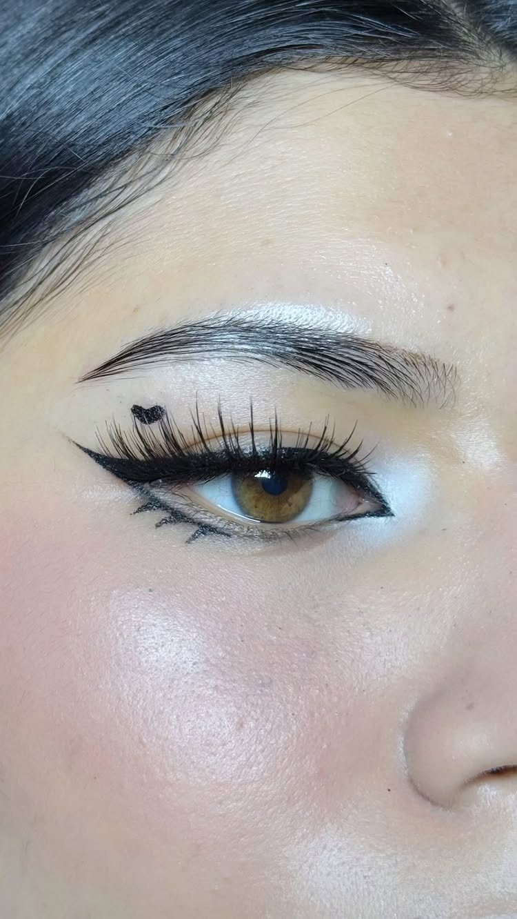 Eye makeup featuring a bold black winged liner with a small heart detail.