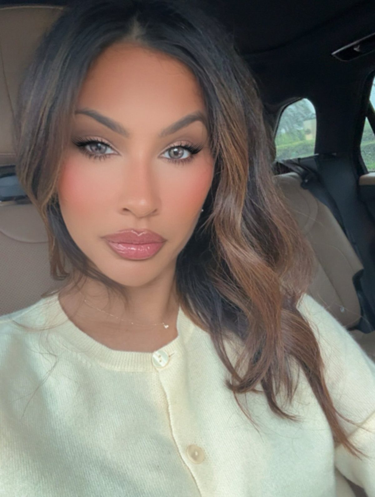 Woman with long brown hair wearing a pale yellow cardigan and soft glam makeup.