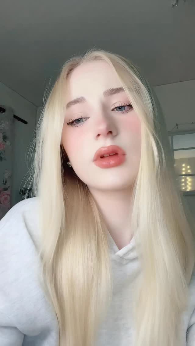 Young woman with long blonde hair and exaggerated plumped lip makeup posing.