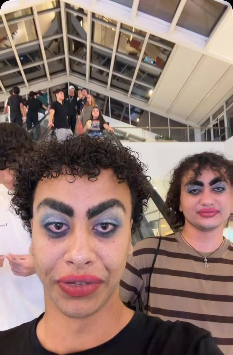 Two people wearing exaggerated blue eyeshadow and thick eyebrows posing for a selfie.