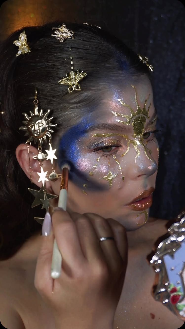 Glitter on Face Ideas: 19 Looks, From Freckles to Skulls 16 Person applying gold and blue glitter makeup with celestial gold hair accessories.